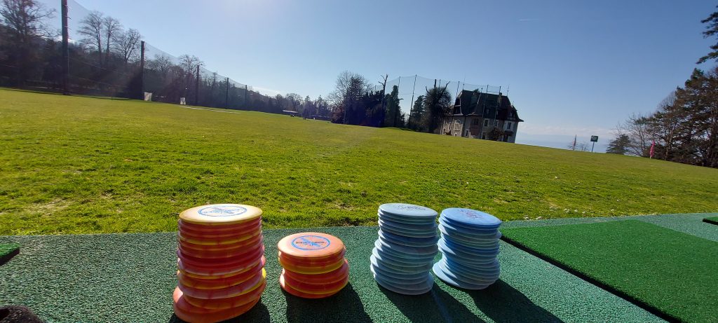 Disques de disc-golf empilés devant un practice
